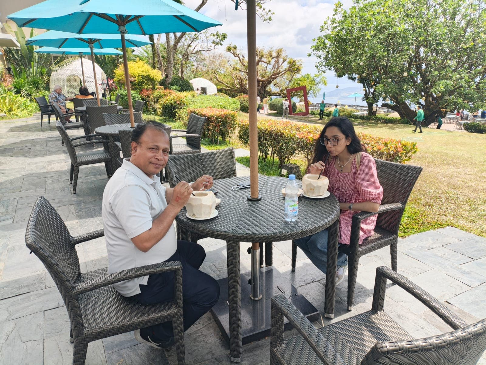 Father and daughter enjoying fresh coconut drinks at an outdoor garden overlooking the scenic landscape of Tagaytay, Philippines.