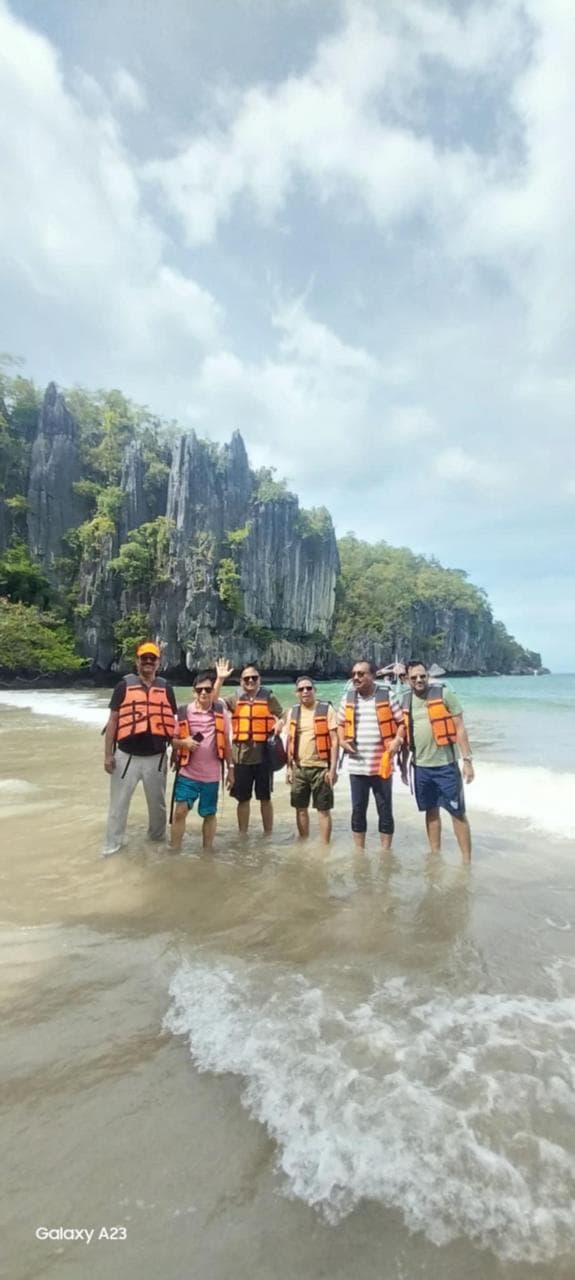 Group of friends wearing life jackets and enjoying the clear waters beside dramatic limestone cliffs in Palawan, Philippines.